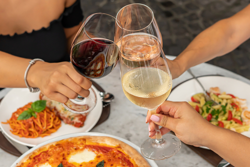 Na imagem, há três mulheres brindando com três taças de vinho
