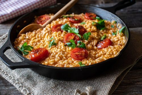 Na imagem, há uma panela com risoto e rodelas de tomate
