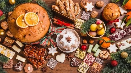Na imagem, há uma ceia de natal italiana com pandoro, doces, biscoitos, frutas e pães