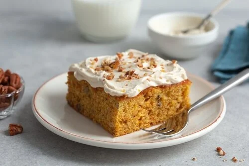 Na imagem, há um pedaço de carrot cake bolo de cenoura com cobertura de chantilly