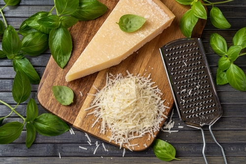 Na imagem, há uma tábua com queijo parmesão parmigiano reggiano em peça e ralado