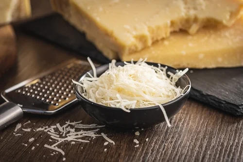 Na imagem, há um potinho preto com queijo parmesão ralado