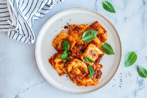 Na imagem, há um prato cheio de ravioli recheado com molho bolonhesa
