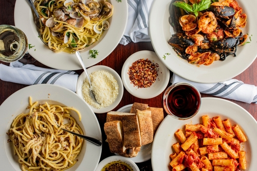 Na imagem, há uma mesa com vários pratos com massas e comidas italianas